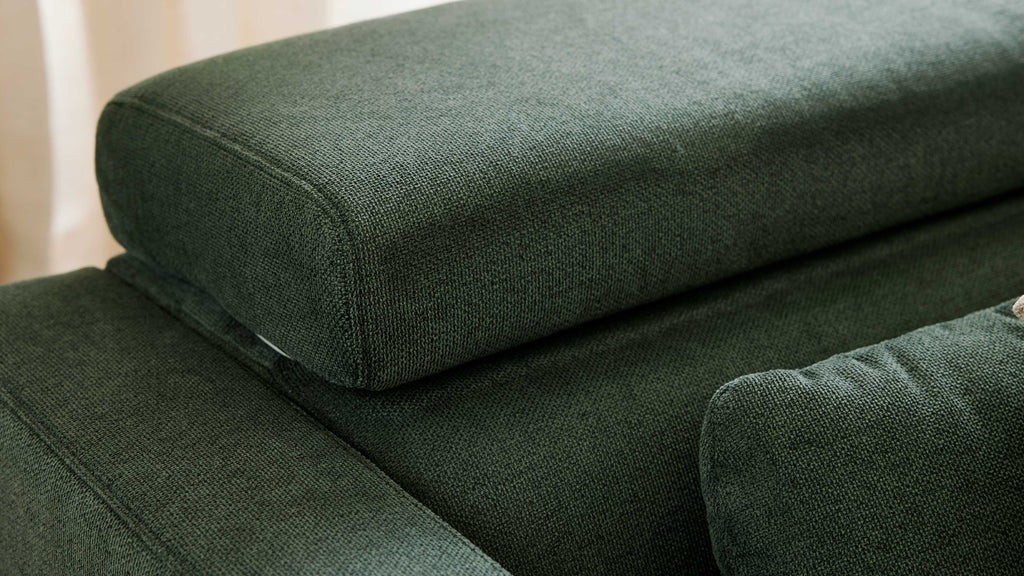 Nahaufnahme eines dunkelgrünen Sofas mit grob gewebtem Bezugsstoff, sichtbaren Nähten und gestapelten Rücken- und Sitzpolstern.