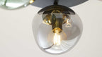 Deckenleuchte mit rauchig-transparentem Glasballon, sichtbarer warm leuchtender Filament-Glühbirne und goldfarbenem Fassungsdetail.