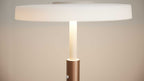 Tischlampe mit flachem weißen Schirm, zentralem opal-weißem Leuchtstab und bronzefarbenem zylindrischem Fuß mit sichtbarer Schraube.