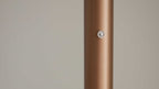 Zylindrische, bronzefarbene, matte Metallstange rechtsseitig mit einem kleinen runden Metallknopf und einfarbigem hellgrauem Hintergrund.