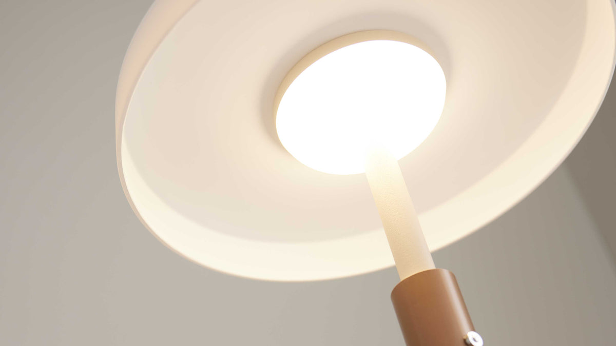 Nahaufnahme einer Lampe mit rundem, leuchtendem Diffusor, weißem weit ausgespanntem Schirm, hellem Schaft und braunem Zylinder am Fuß.