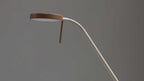 Schreibtischlampe mit rundem braunem Lampenschirm und weißem, gebogenem Schwanenhals sowie langem Stabarm vor grauem Hintergrund.