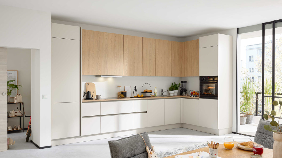 Helle Küchenzeile mit Holzfronten, modern und schlicht, ausgestattet mit Herd, Spüle, Kaffeemaschine und Obstschale.