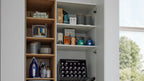 Offener Schrank mit Holzregalen links (Bügeleisen, Flaschen, Schalen, Drahtkorb) und rechten Regalböden mit Dosen, Kartons und Bierkiste.