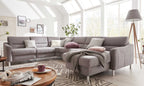 Eine graue L-förmige Couch mit verschiedenen Kissen und einer Decke, umgeben von einem runden Tisch und einer Stehlampe.