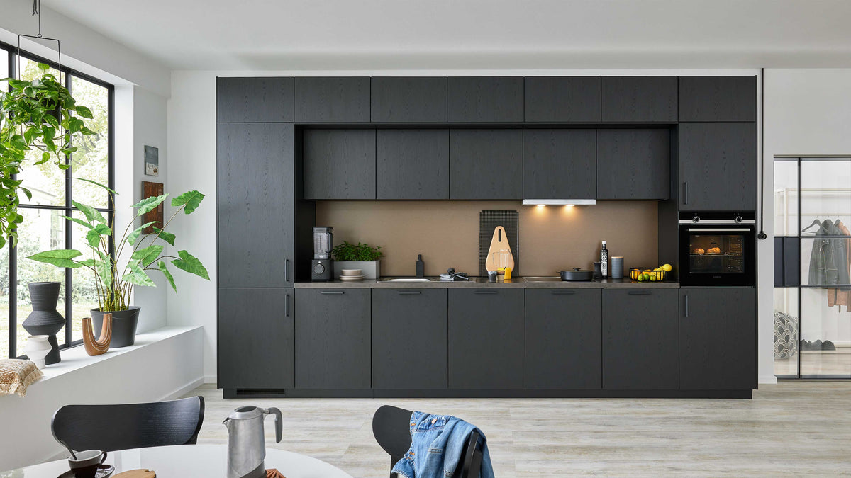 Moderne Einbauküche in dunkler Holzoptik mit einer Arbeitsplatte, einem Herd, einer Spüle und einem Backofen, ergänzt von Pflanzen und Küchenutensilien.
