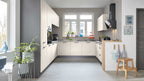 Moderne Küche mit hellen, schlichten Fronten, grauen Wänden, einer Arbeitsfläche, Pflanzen und einem Holzstuhl in der Ecke.
