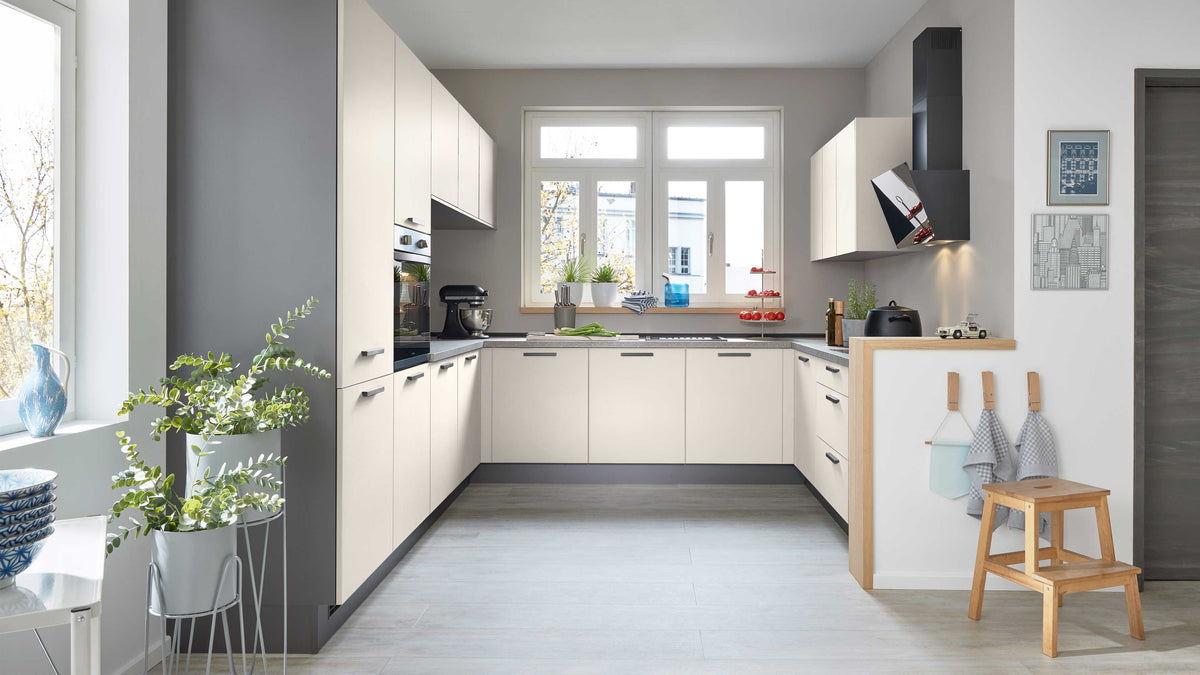 Moderne Küche mit hellen, schlichten Fronten, grauen Wänden, einer Arbeitsfläche, Pflanzen und einem Holzstuhl in der Ecke.