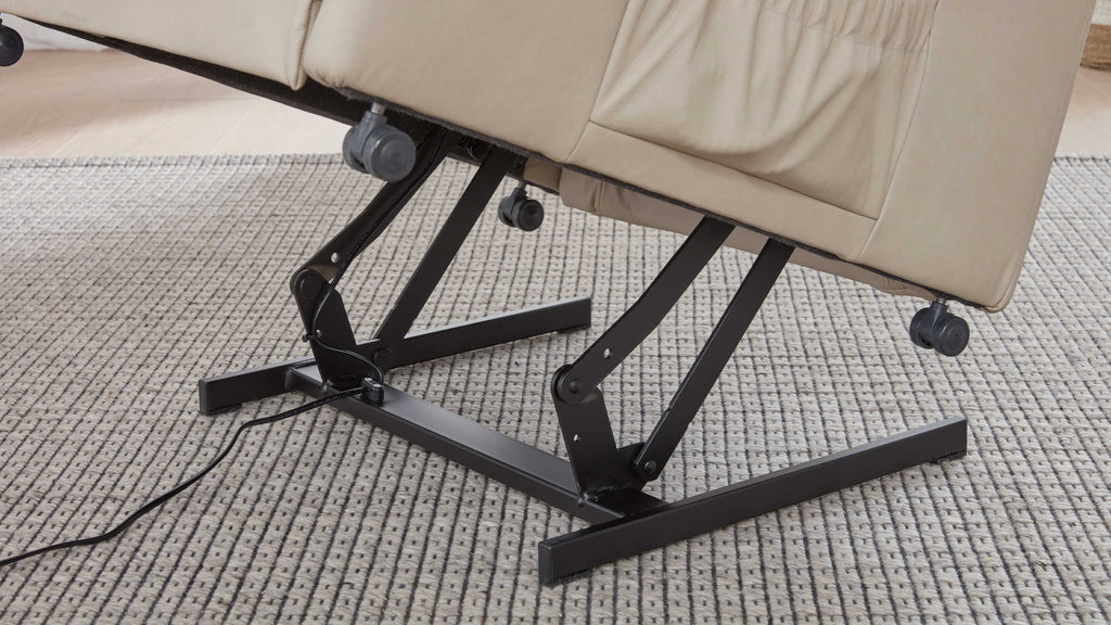 Ein beige gepolsterter Sessel mit einem schwarzen Metallgestell und einem Mechanismus zur Neigungsverstellung steht auf einem hellen, gewebten Teppich.