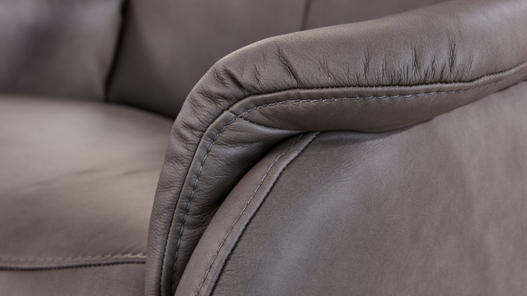 Nahaufnahme eines grauen Ledersofas, das den gepolsterten Armlehnenbereich mit sichtbarer Naht und leicht geprägter Oberfläche zeigt.