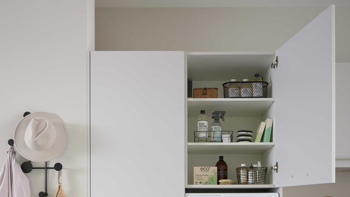 Der weiße Schrank zeigt geöffnete Türen mit verschiedenen Flaschen, Körben und einer Schachtel auf mehreren Regalen.