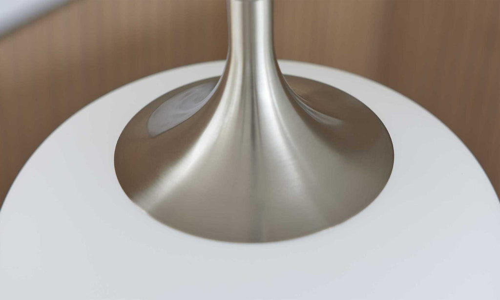 Die Detailaufnahme zeigt die Basis einer Lampe mit einem glänzenden, metallischen Fuß und einem weißen, runden Lampenschirm.