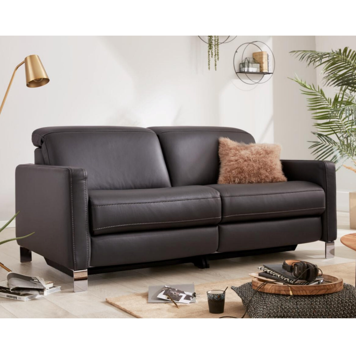 HUKLA® | IL Interliving Serie 4054 Ledersofa in Anthrazit mit einem braunen Kissen, Büchern, Pflanzen und einem Couchtisch daneben.