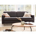 Hinter einem runden Couchtisch steht ein Sofa der HUKLA® IL Interliving Serie 4054 in Leder Anthrazit mit zwei Plüschkissen.