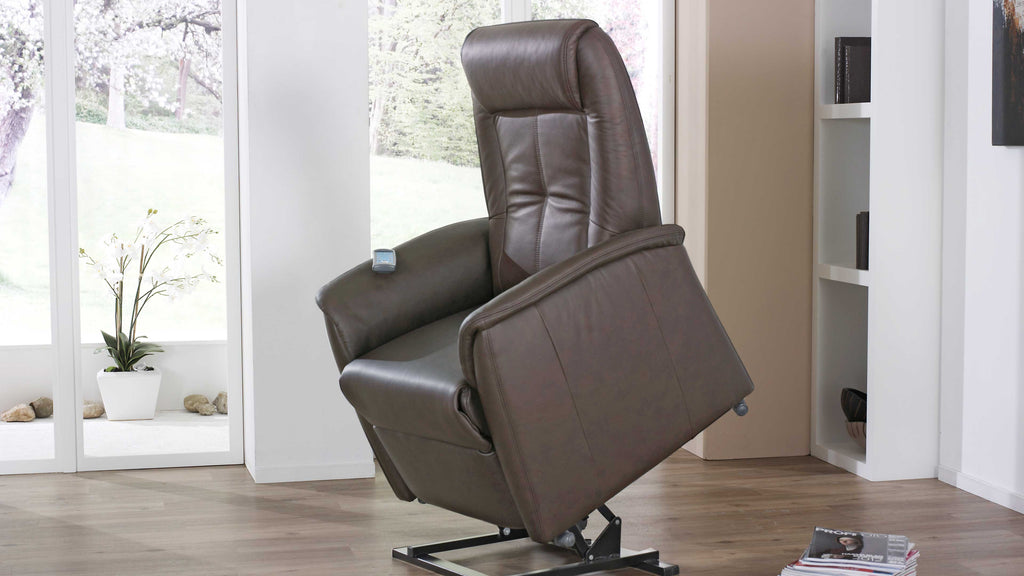 Ein brauner Relaxsessel mit elektrisch verstellbarer Rückenlehne steht in einem hellen Raum, neben einem Pflanzenkübel und einem Regal.