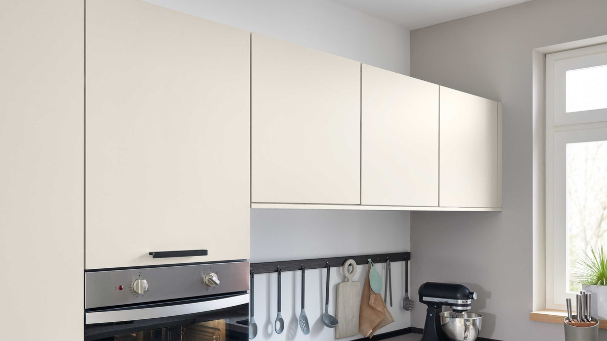 Hängeschränke in hellem Farbton über einem Backofen mit Bedienelementen, darunter eine Wand mit Küchenutensilien und einem Mixer.