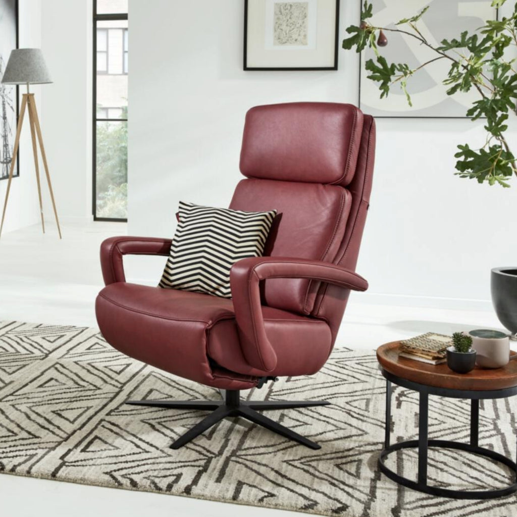 Ein roter HUKLA® | IL-Sessel aus der Interliving-Serie 4541 auf einem gemusterten Teppich mit einem gestreiften Kissen in einem modernen Wohnzimmer.