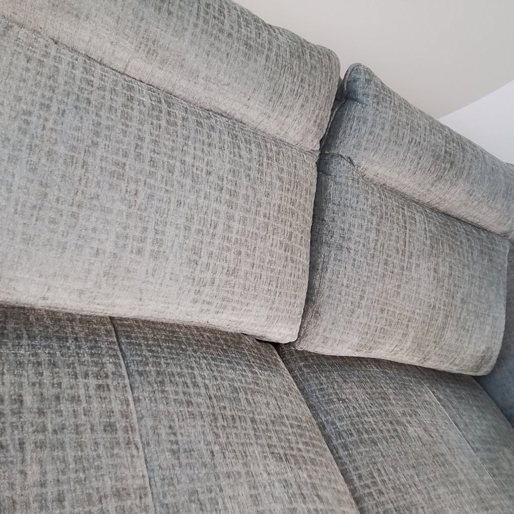 Nahaufnahme des 3-Sitzer-Sofas „Habufa“ 49553 „Valletta“ von 0176, grau mit zwei Rückenkissen, vor einer weißen Wand.