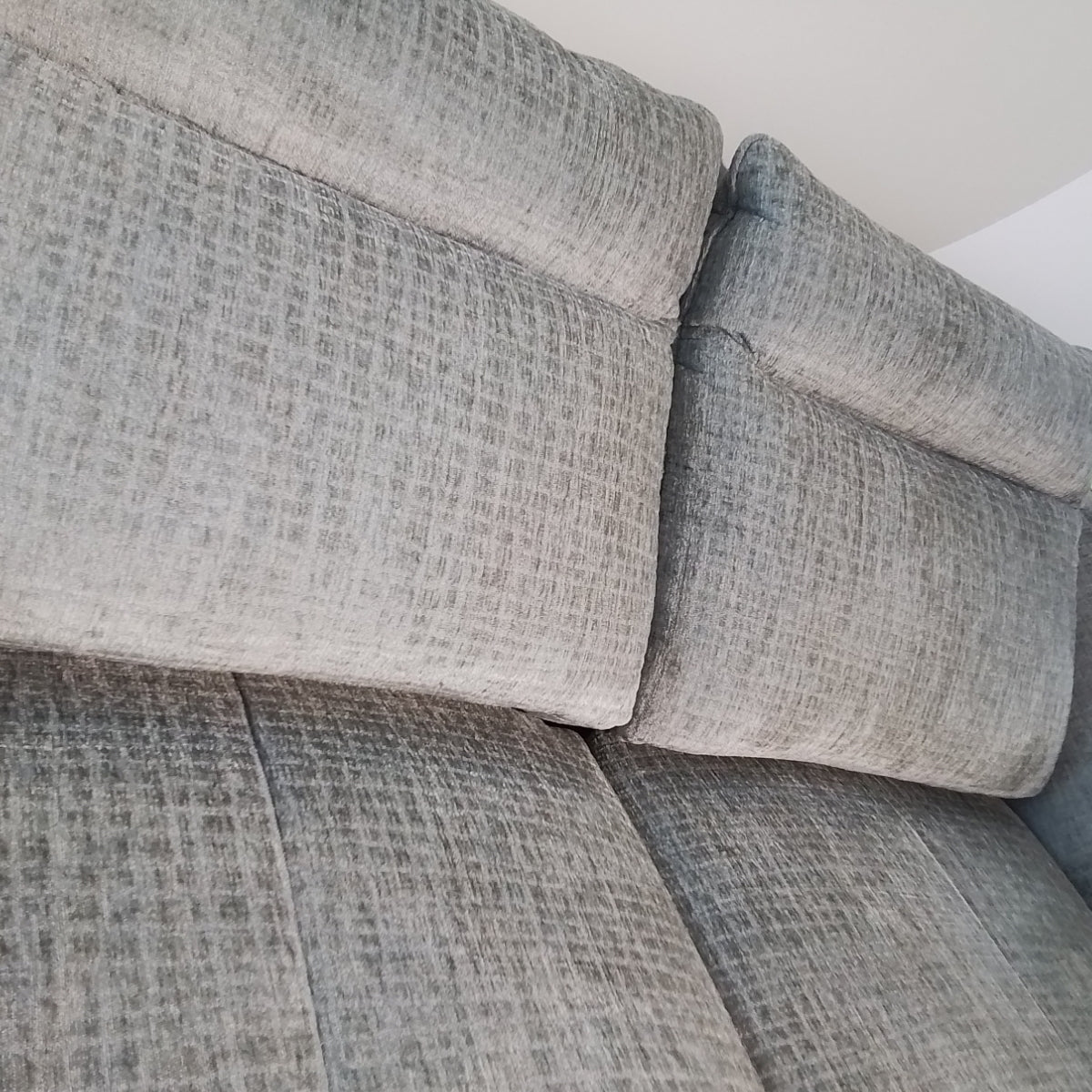 Nahaufnahme des 3-Sitzer-Sofas „Habufa“ 49553 „Valletta“ von 0176, grau mit zwei Rückenkissen, vor einer weißen Wand.
