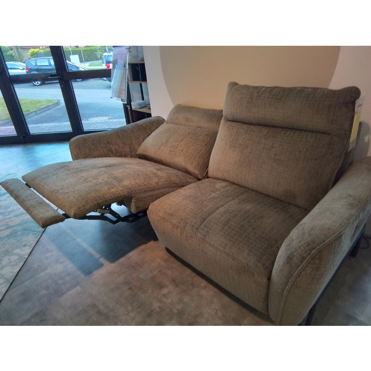 Habufa 3-Sitzer-Sofa „Valletta“ von 0176, brauner Liegesessel mit ausgeklappter Fußstütze, abgebildet in einem Innenraum vor großen Fenstern.