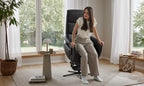 Eine Frau sitzt in einem hellen Raum vor großen Fenstern im HUKLA® | IL Relaxsessel der Interliving-Serie 4545 aus Glattleder.