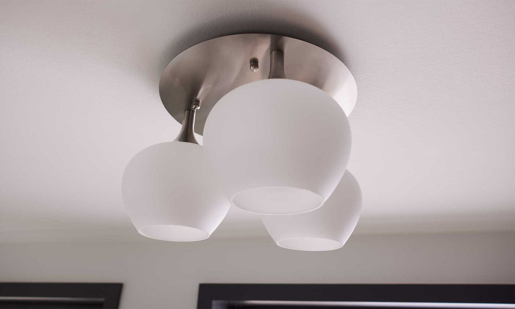 Decke mit einer runden Deckenlampe, die drei mattierte Glaskugeln in Weiß hält, montiert an einer silbernen Halterung.