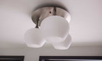Decke mit einer runden Deckenlampe, die drei mattierte Glaskugeln in Weiß hält, montiert an einer silbernen Halterung.