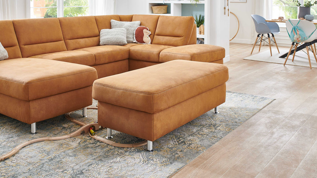 Große, hellbraune ZEHDENICK Modulmaster MM-ZE1049 Ottomane vor einem passenden Ecksofa auf einem gemusterten Teppich.