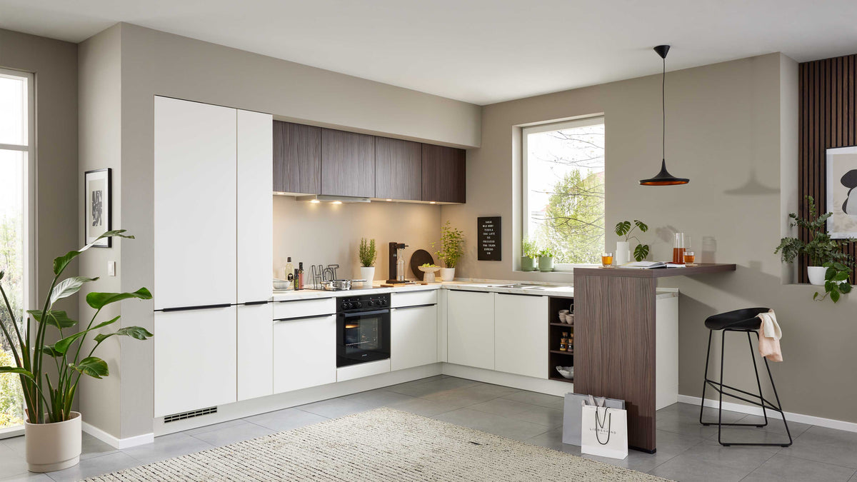 Moderne Küche mit weißen Fronten, Holzregal, einem Bartisch, modernen Barhockern und Pflanzen, zusätzlich Beleuchtung über der Arbeitsfläche.