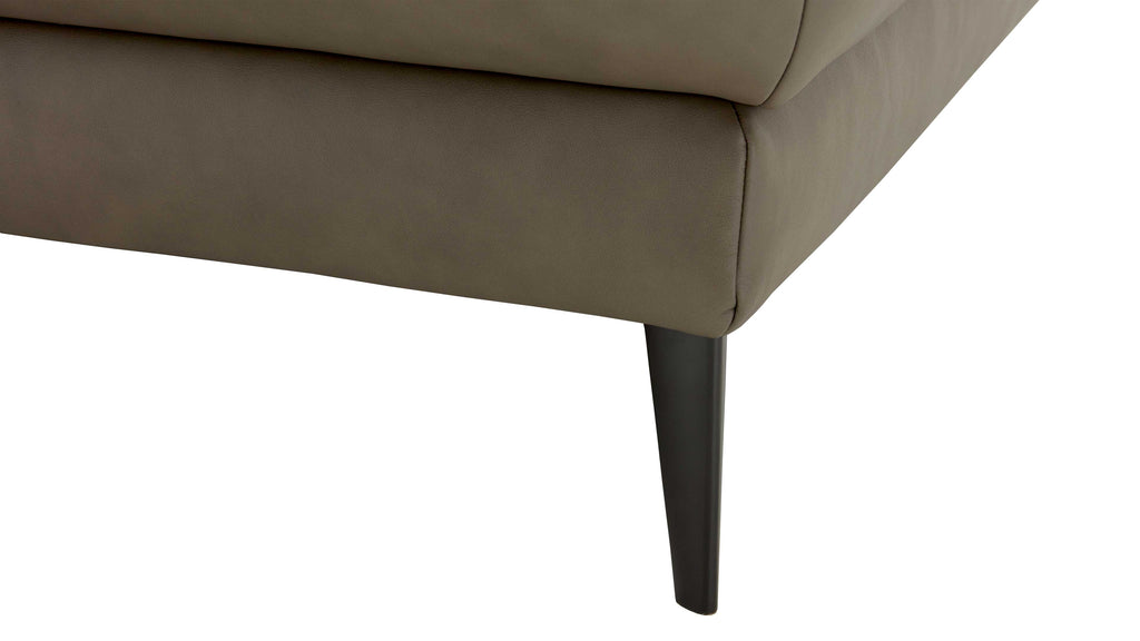 Die untere Ecke eines beigefarbenen Polstermöbels mit einem schmalen, schwarzen Holzbein.