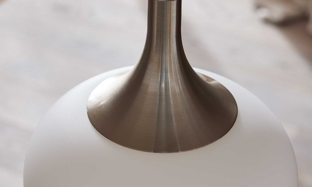 Sicht auf den oberen Teil einer Lampe mit einem glänzenden, metallischen Fuß und einem runden, matten Lampenschirm in Weiß.