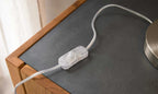 Ein transparenter Schalter mit Kabel liegt auf einer grauen Tischplatte, umgeben von Holzverkleidung.