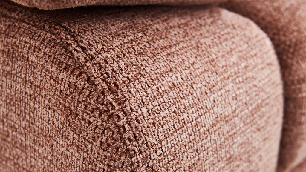 Nahaufnahme eines Möbelstücks mit einer strukturierten, rosafarbenen Stoffoberfläche, die eine weiche Textur zeigt.