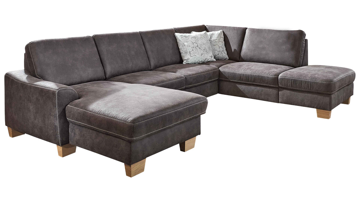 Ecksofa in dunkelgrauem Stoff mit drei Rückenlehnen, einer Ottomane und einem dekorativen Kissen in hellen Farben, auf Holzfüßen.