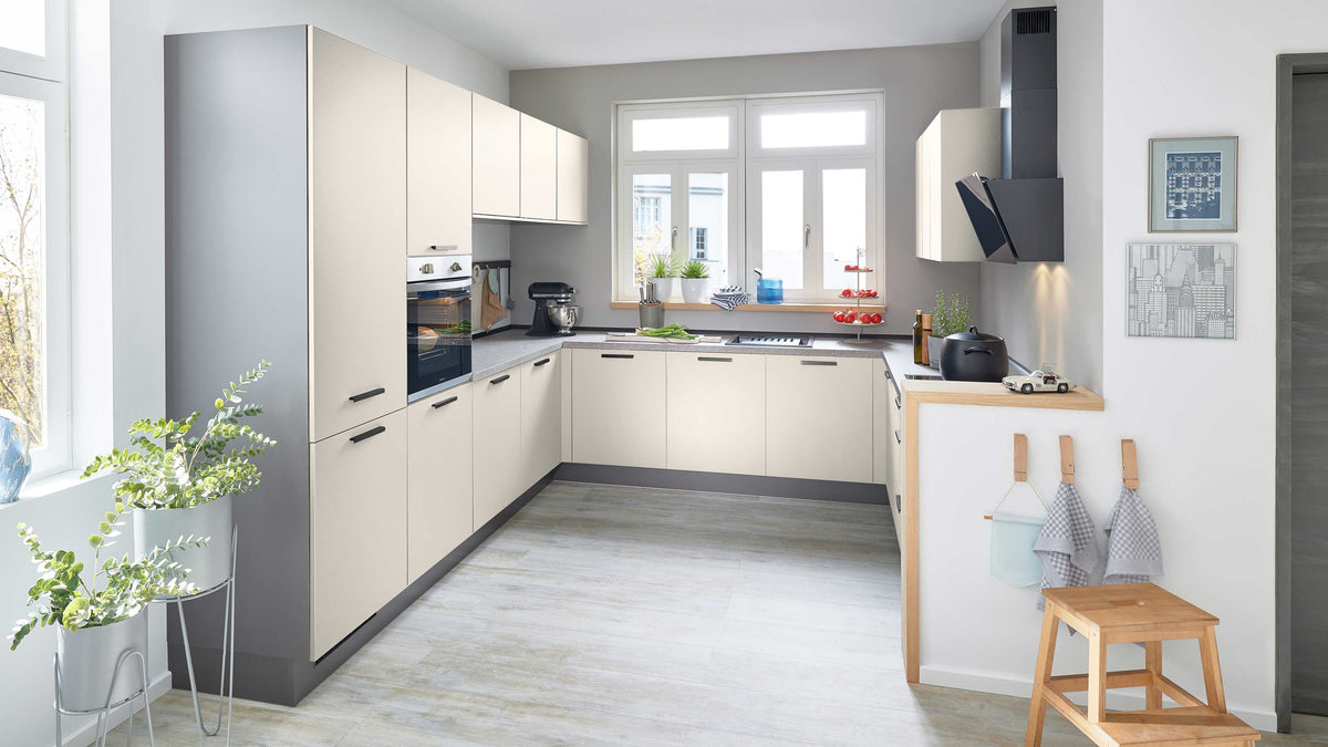Moderne, helle Küche mit hellgrauen und weißen Möbeln, ausgestattet mit Herd, Spüle, Pflanzen und Holzregal.