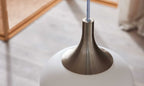 Hängelampe mit einem glatten, weißen Lampenschirm und einem metallischen, glanzvollen Lampenstiel.