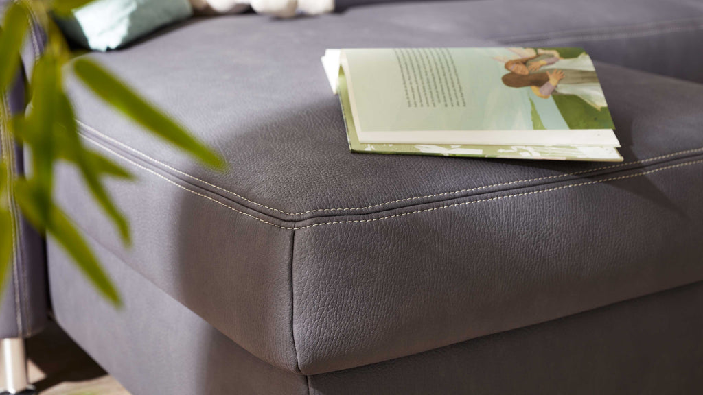 Ein graues Modulmaster MM-ZE1049-Ecksofa aus Leder mit weißen Kontrastnähten und einem aufgeschlagenen Buch auf der Sitzfläche.