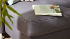 Ein graues Modulmaster MM-ZE1049-Ecksofa aus Leder mit weißen Kontrastnähten und einem aufgeschlagenen Buch auf der Sitzfläche.