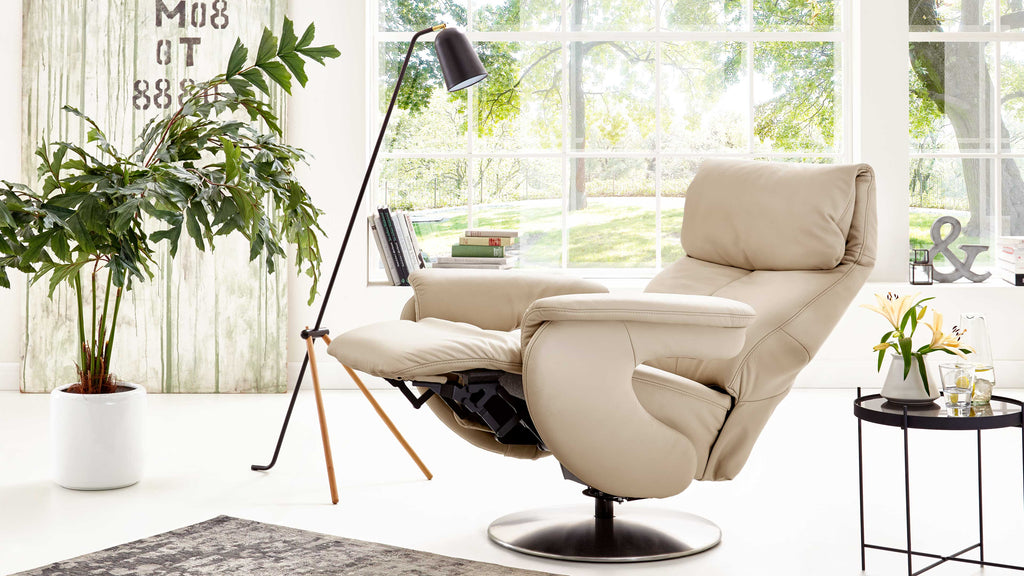 Beiges Leder, Himolla Comfortmaster 7304 – Easy-Swing-Sessel 31N auf einem Sockel neben einer Stehlampe und einem Beistelltisch.
