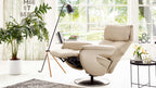 Beiges Leder, Himolla Comfortmaster 7304 – Easy-Swing-Sessel 31N auf einem Sockel neben einer Stehlampe und einem Beistelltisch.