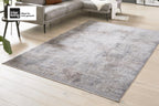 Eleganter GOLZE | Der Teppich IL G-8050 in Grau/Sand mit Allover-Muster auf einem Holzboden vor einem grauen Sofa.