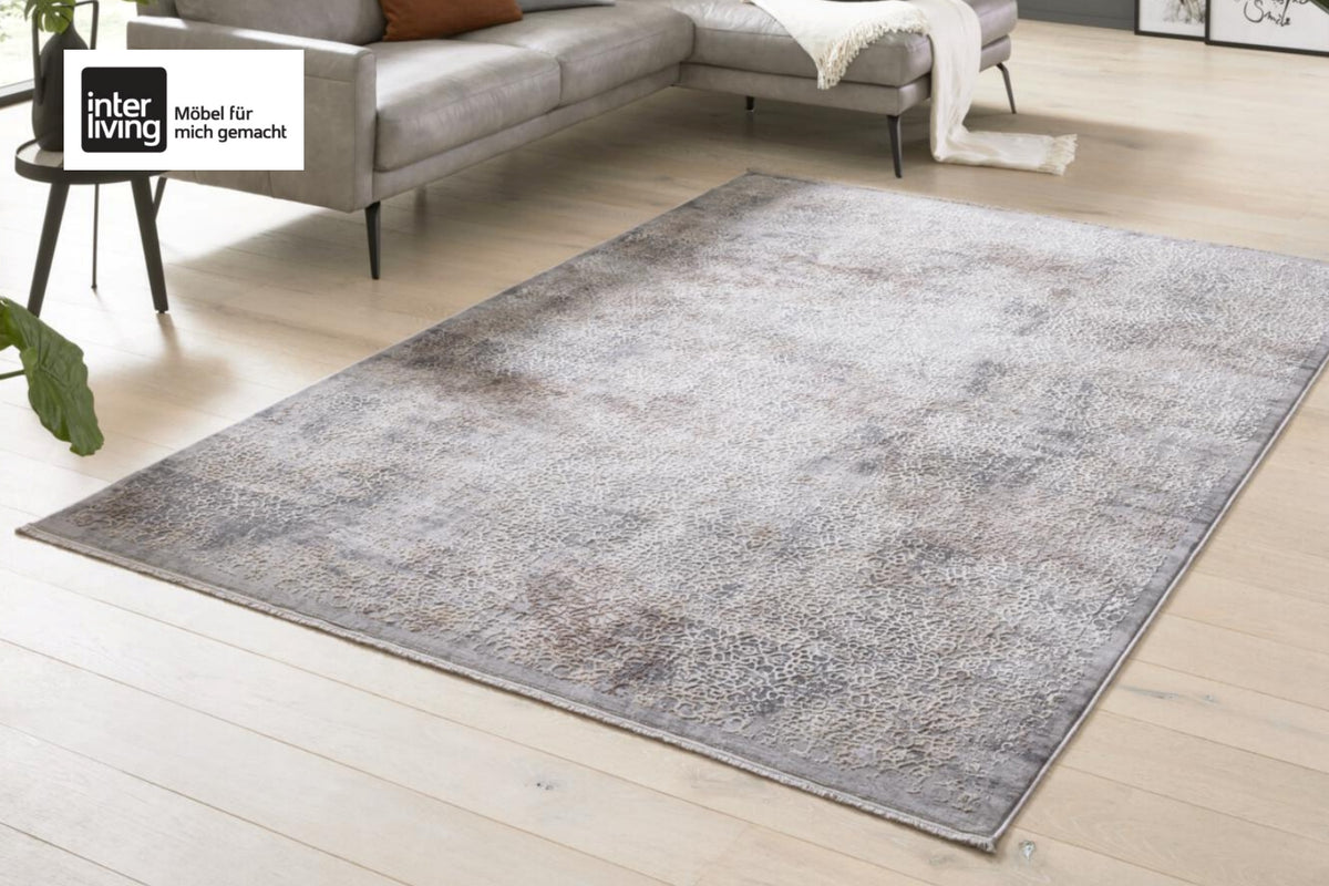 GOLZE | Der Teppich in Grau/Sand mit Allover-Muster neben einem grauen Sofa und einem schwarzen Tisch auf einem Holzboden.