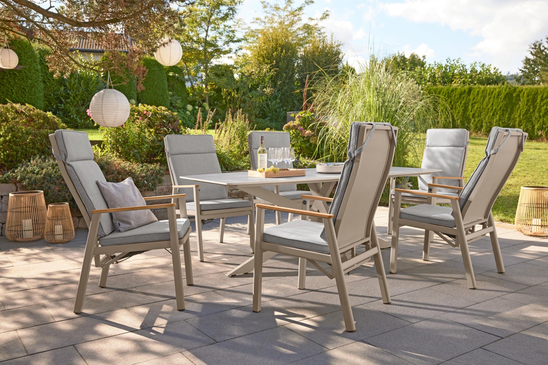 Gartentischgruppe mit gepolsterten Stühlen auf einer Terrasse, auf dem Tisch stehen Wein und Weingläser.