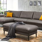 Modernes Wohnzimmer mit grauem Ecksofa, HUKLA® XXL-Hocker, gelben Kissen, einer Überwurfdecke und Wandbildern.