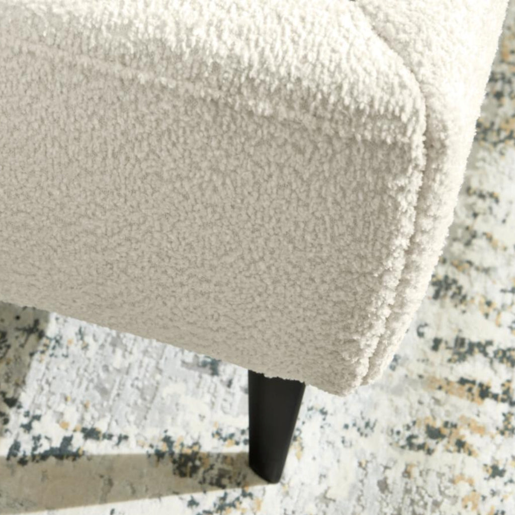 Nahaufnahme einer cremefarbenen Bettecke der HUKLA® Interliving Serie 1416 mit schwarzem Fuß auf einem grau-weiß gemusterten Teppich.