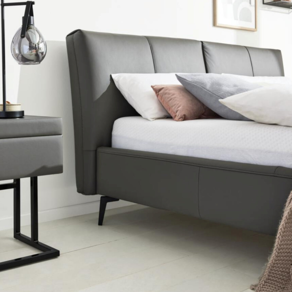 HUKLA® Interliving Serie 1416 Lederpolsterbett 180 × 200 cm in Anthrazit mit Nachttisch und Lampe.