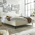 Modernes Schlafzimmer mit dem HUKLA® Interliving Serie 1416 Polsterbettgestell „Kama“ in Naturweiß, einer braunen Decke, Kunstwerken und Pflanzen.