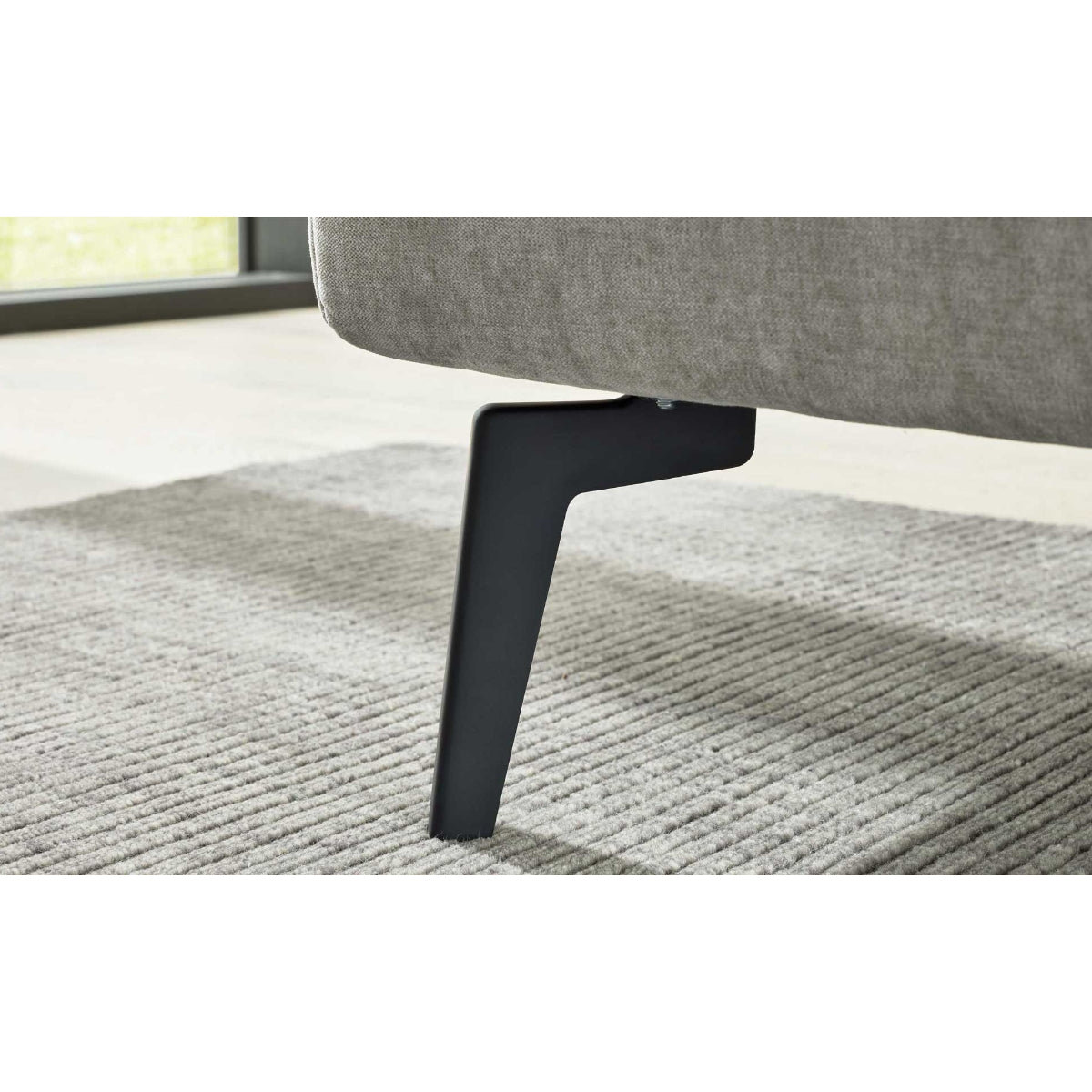 Schwarzes Metallsofabein auf grauem Teppich unter einem HUKLA® Interliving Serie 1416 Polsterbettgestell, Balu Silver, 180 x 200 cm.