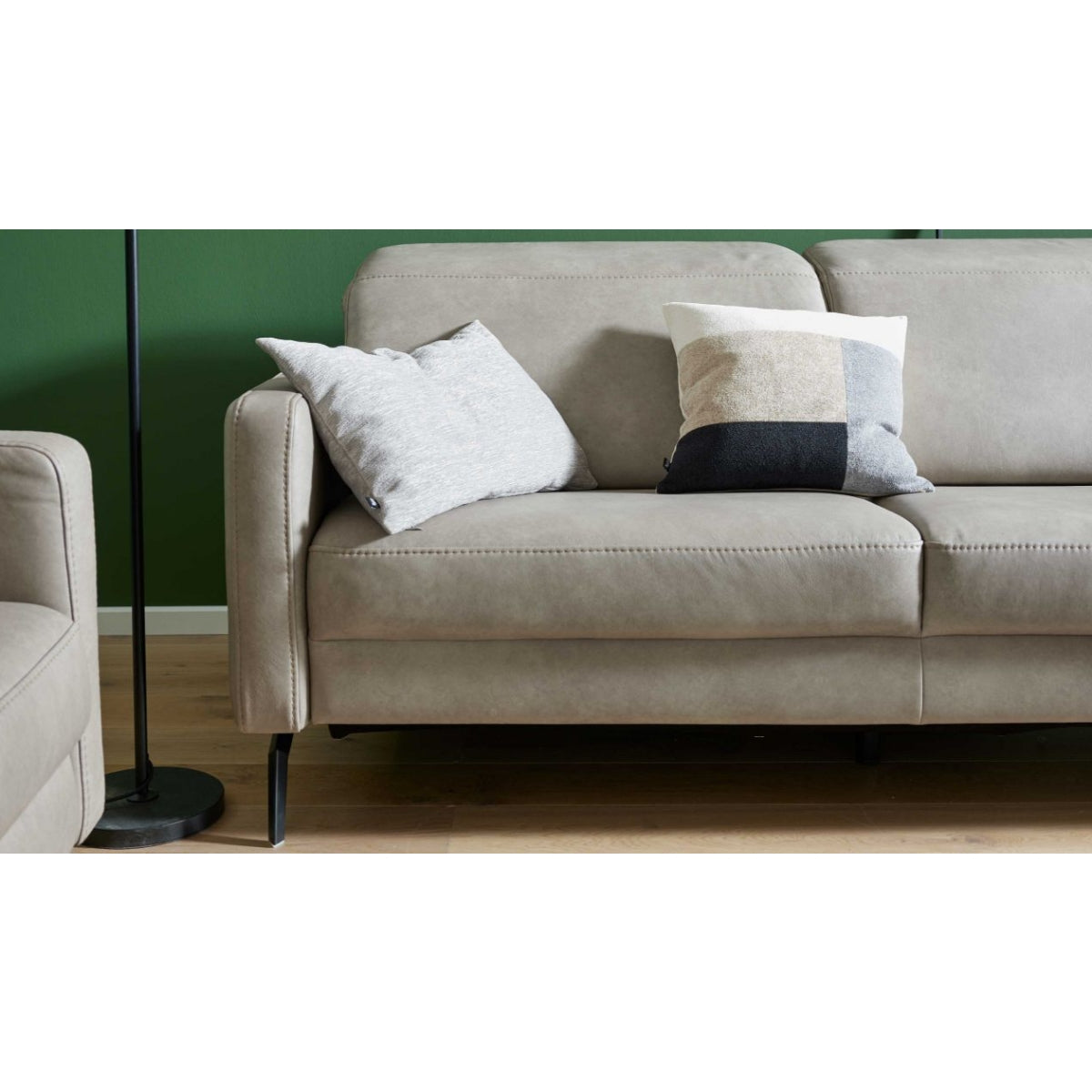 HUKLA® | IL Interliving Serie 4065 2,5-Sitzer aus „Cloudy Gravel“-Leder mit zwei Kissen, auf Holzboden vor einer grünen Wand.