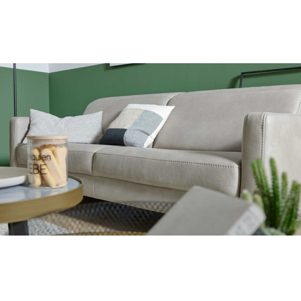HUKLA® | IL Interliving Serie 4065 2,5-Sitzer-Sofa „Cloudy“ in Kieseloptik mit drei Kissen, Kerze auf dem Tisch, grün-weiße Wand.